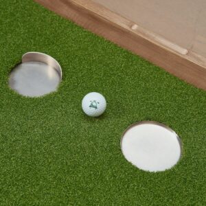 Golf ball next to two cups on a putting green